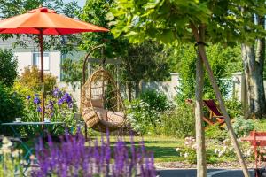 un columpio y una sombrilla en un jardín con flores púrpuras en La Ressourçante, en Puisieulx