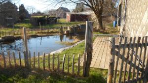 una valla de madera junto a un estanque junto a una casa en La Vannerie en Havelange