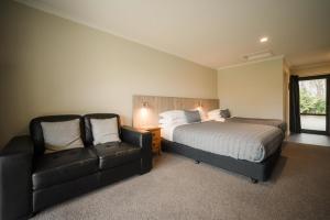 a bedroom with a bed and a couch and a chair at Invercargill Holiday Park & Motels in Invercargill