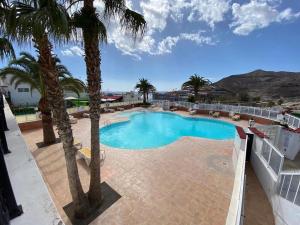 a large swimming pool with palm trees on a balcony at Sunset Balcony with Ocean Views and pool access in Mogán
