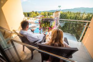 un hombre y una mujer sentados en un balcón con vistas a una piscina en Terme Paradiso - Hotel Paradiso, en Dobova