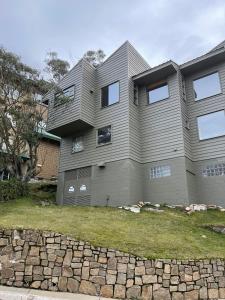 a house with a stone wall in front of it at Winterbrook Chalet in Mount Buller