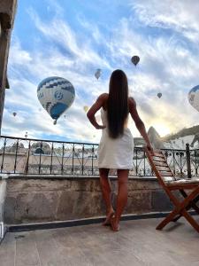 a woman standing on a ledge looking at hot air balloons at Angel Cave Suite in Göreme