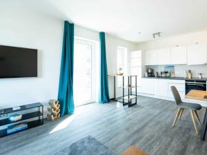 a living room with a table and a kitchen with blue curtains at Hafenspitze App 36 in Wismar