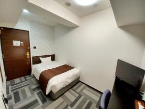 Akasaka Urban Hotel Annex في طوكيو: غرفة نوم صغيرة بها سرير وتلفزيون