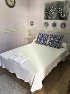 1 cama blanca con almohadas azules y reloj en la pared en Venta de Abajo, en El Castillo de las Guardas