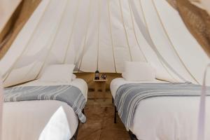 two beds in a tent with white sheets at Under Canvas Moab in Moab