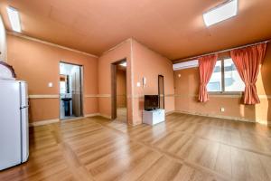 an empty living room with wooden floors and a tv at Lohas Pension in Seogwipo