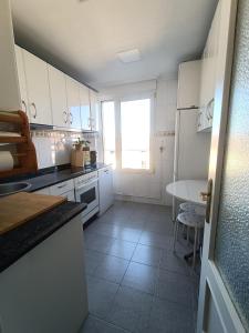 cocina con armarios blancos, mesa y ventana en Bonito duplex cerca de la playa y de Santander, en Santa Cruz de Bezana