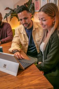 a man and woman sitting at a table with a laptop at The Corner London City in London