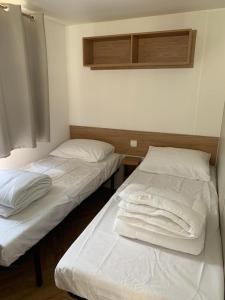 two beds in a room with white sheets and pillows at Mobil home BASSET au camping à St Hilaire de Riez 400m de la mer in Saint-Hilaire-de-Riez