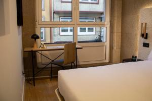 a bedroom with a bed and a desk and a window at Hotel Alda Orzán in A Coruña