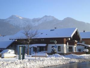 a building covered in snow with mountains in the background at Ferienwohnung Kreuz in Grassau