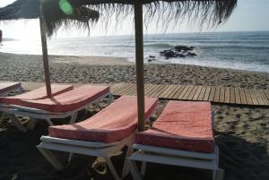 zwei Liegestühle und ein Sonnenschirm am Strand in der Unterkunft Apartamentos La Dorada in La Cala de Mijas