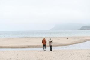 two people standing on a beach with a surfboard at Marine Hotel Ballycastle in Ballycastle