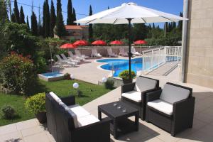 un patio con sillas, una sombrilla y una piscina en Apartments Grand Pinea, en Čilipi