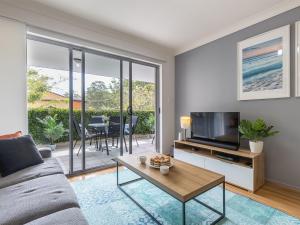 a living room with a couch and a tv and a table at Mikalex 10 2 Shoal Bay Road Nelson Bay in Nelson Bay