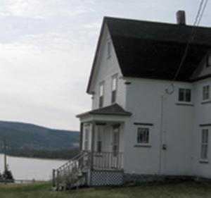a white house with a black roof next to a lake at Margaree Harbour View Inn B&B in Margaree Harbour