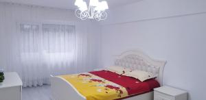 ein weißes Schlafzimmer mit einem Bett mit einer roten und gelben Decke in der Unterkunft White Apartament, Brăila in Brăila