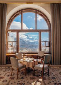 Cette chambre dispose d'une grande fenêtre et d'une table avec des chaises. dans l'établissement Suvretta House, à Saint-Moritz