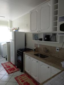 eine Küche mit weißen Schränken, einer Spüle und einem Kühlschrank in der Unterkunft Apto. 2 quartos em Bombinhas (60 m da praia) in Bombinhas