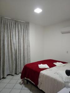 a bedroom with a bed with a red blanket and a window at Apto. 2 quartos em Bombinhas (60 m da praia) in Bombinhas