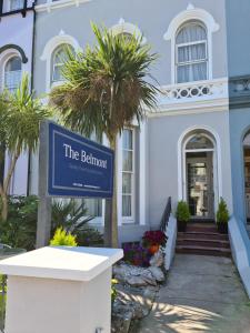 a sign in front of a white building with palm trees at The Belmont in Torquay