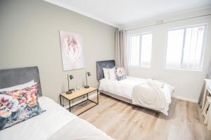 a white bedroom with two beds and a table at Plettenberg Bay Unit 2 Greenpoint Mews Apartment with Backup Power in Plettenberg Bay +23 photos