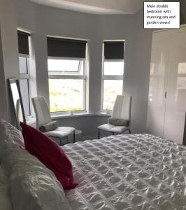 a bedroom with a bed and two chairs and windows at Apartment 3, 2 Antrim Gardens, Portrush in Portrush