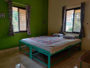 Cama en habitación verde con 2 ventanas en Sakhey Homestay, en Ratnagiri
