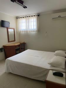 a bedroom with a large white bed and a desk at Regio Plaza Hotel in Ourinhos