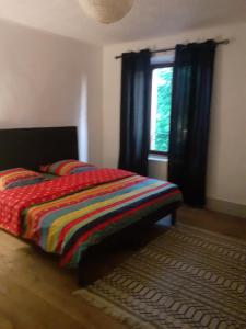 ein Schlafzimmer mit einem Bett mit einer bunten Decke und einem Fenster in der Unterkunft Résidence de Suzanne Gîte avec sauna privatif in Brommat