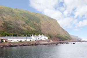 una casa al lado de una colina al lado del agua en The Cottage By The Sea, Scotland, en Burnmouth