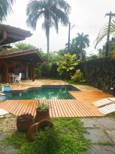 a pool with a wooden deck next to a house at Casa 5 suítes com piscina e churrasqueira in Ubatuba