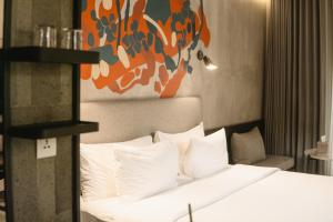 a bedroom with a bed with white pillows and an orange painting at ARTOTEL Haniman Ubud in Ubud