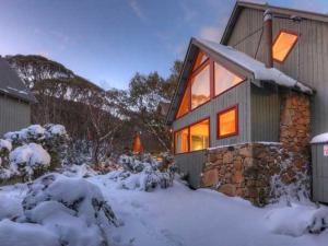 een huis bedekt met sneeuw met de lichten aan bij Snowy Chalet in Thredbo
