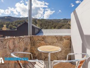 a table and chairs on a balcony with a stone wall at Squatters Run 14 in Thredbo