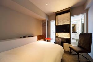 a bedroom with a bed and a chair and a window at remm Kagoshima in Kagoshima
