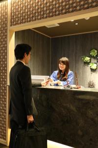 mężczyzna i kobieta stojący przy ladzie w obiekcie Cabin & Capsule Hotel J-SHIP Osaka Namba w Osace