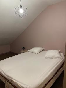 Una cama blanca con dos almohadas encima. en Appartement 14 couchages vallée du Grésivaudan, en La Buissière