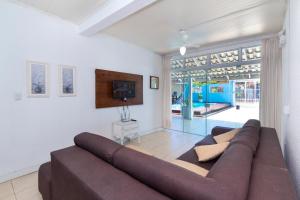 a living room with a brown couch and a tv at CASA COM PISCINA EM MORRINHOS - RUA HORTÊNCIA in Bombinhas