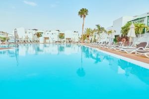 une grande piscine avec des chaises et des palmiers dans l'établissement Gloria Izaro Club Hotel, à Puerto del Carmen