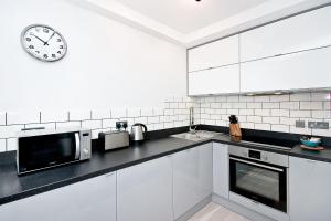 une cuisine blanche avec une horloge sur le mur dans l'établissement Heinze Flat 402 - One bedroom fourth floor flat By City Living London, à Londres