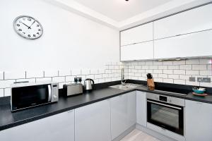 eine weiße Küche mit einer Uhr an der Wand in der Unterkunft Heinze Flat 402 - One bedroom fourth floor flat By City Living London in London