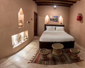 1 dormitorio con 1 cama y 2 taburetes sobre una alfombra en Bait Alharah, en Al Jināh