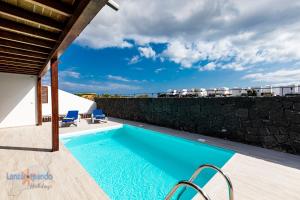 basen z 2 niebieskimi krzesłami obok ściany w obiekcie Vivienda Vacacional Del Mar w mieście Playa Blanca