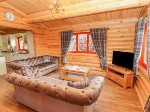 a log cabin living room with a couch and a tv at Maple Lodge in Oakham