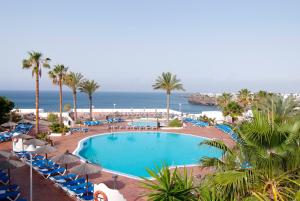 a pool with chairs and umbrellas and the ocean at Sandos Papagayo in Playa Blanca