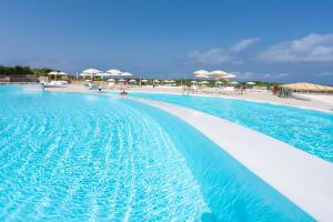 a large swimming pool next to a beach with umbrellas at Amareclub Red Sun Village in Isola Rossa