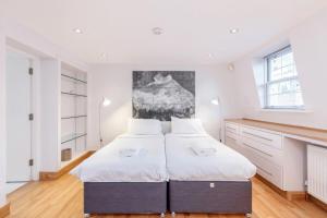 ロンドンにあるBeautiful 1 Bedroom Apartment in Victoriaの白い壁とウッドフロアのベッドルーム1室(ベッド2台付)